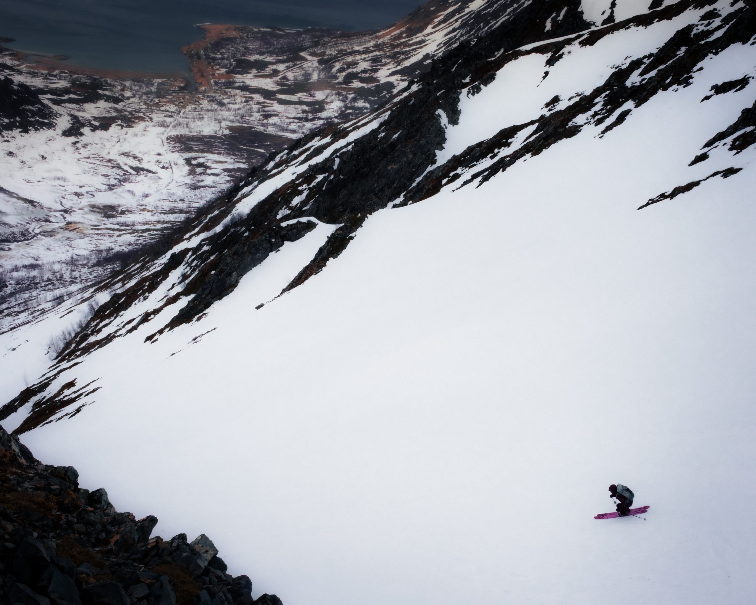 Tiny skier far below dark squall over fjord
